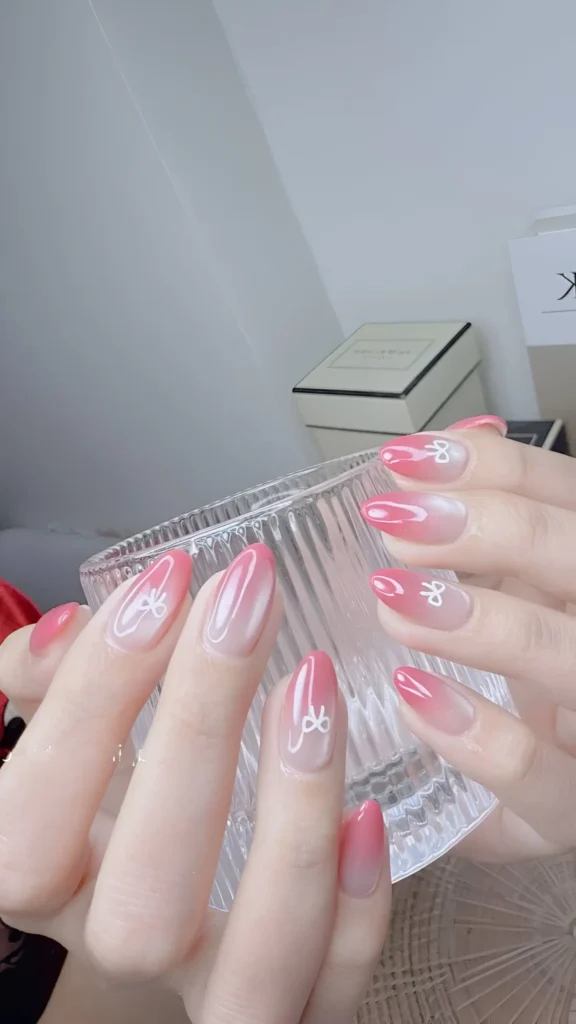 Elegant pink ombré effect on long almond-shaped nails, accented with white bow line art. A pretty, classy nail idea.