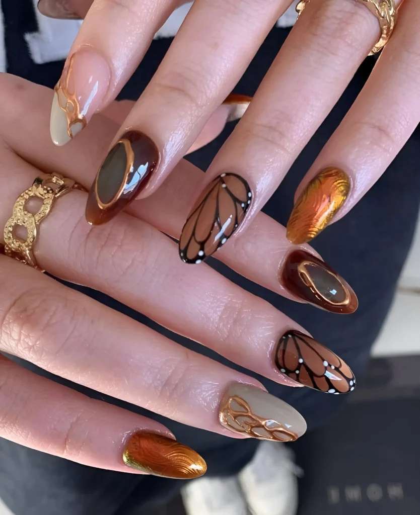 Intricate butterfly wing nail art in brown and black with copper chrome accents on almond nails.