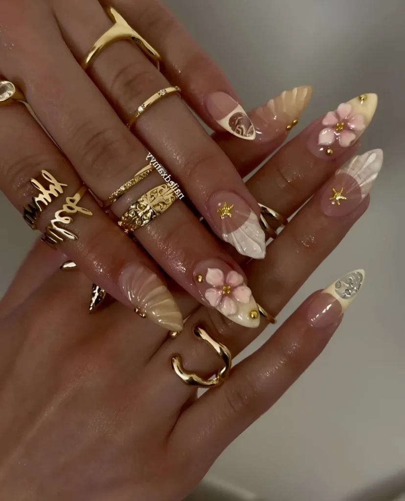 Long stiletto nails with 3D sculpted seashells and pink flowers featuring gold accents, mermaidcore style.