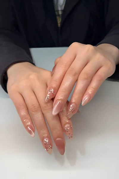 Almond nails with sheer nude base, subtle sparkle accents, and soft magnetic effect for a clean girl look.