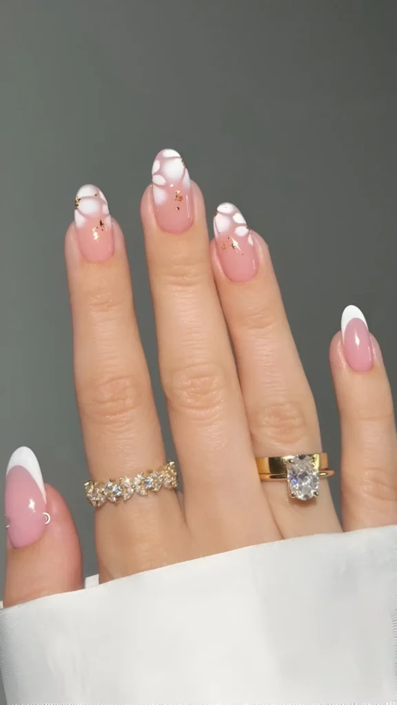 Almond nails with abstract white petal designs and gold flecks over classic French tips, a beautiful classy nail idea.