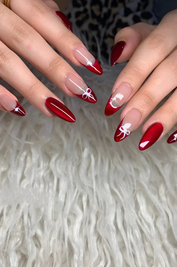 Deep red almond nails featuring French tip variations and white bow nail art.