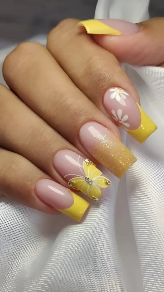 Long square nails with yellow French tips, featuring accent nails with white daisies, a 3D yellow butterfly, and yellow glitter ombré.