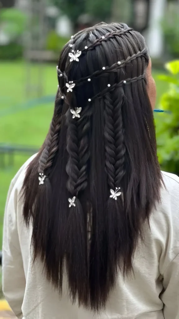 Back view of long dark hair styled with a pearl-accented braided headband, two fishtail braids, and decorative butterfly clips.