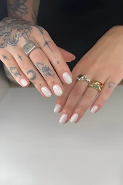 Short rounded nails painted with a glossy milky white clean girl polish.