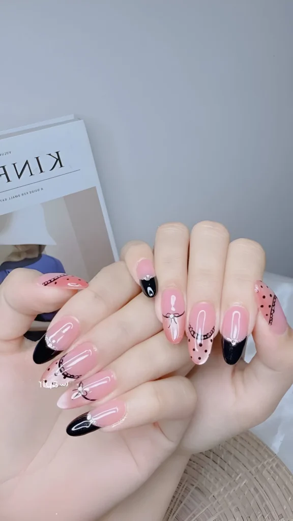 Chic mix-and-match nail art on a sheer nude base: black French tips, bows, chains, and polka dots on almond nails. A versatile classy nail design.