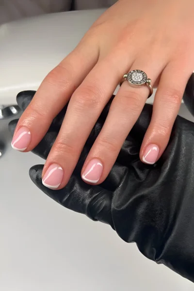 Short square nails with a delicate French manicure featuring a sheer pink base and thin white tips.