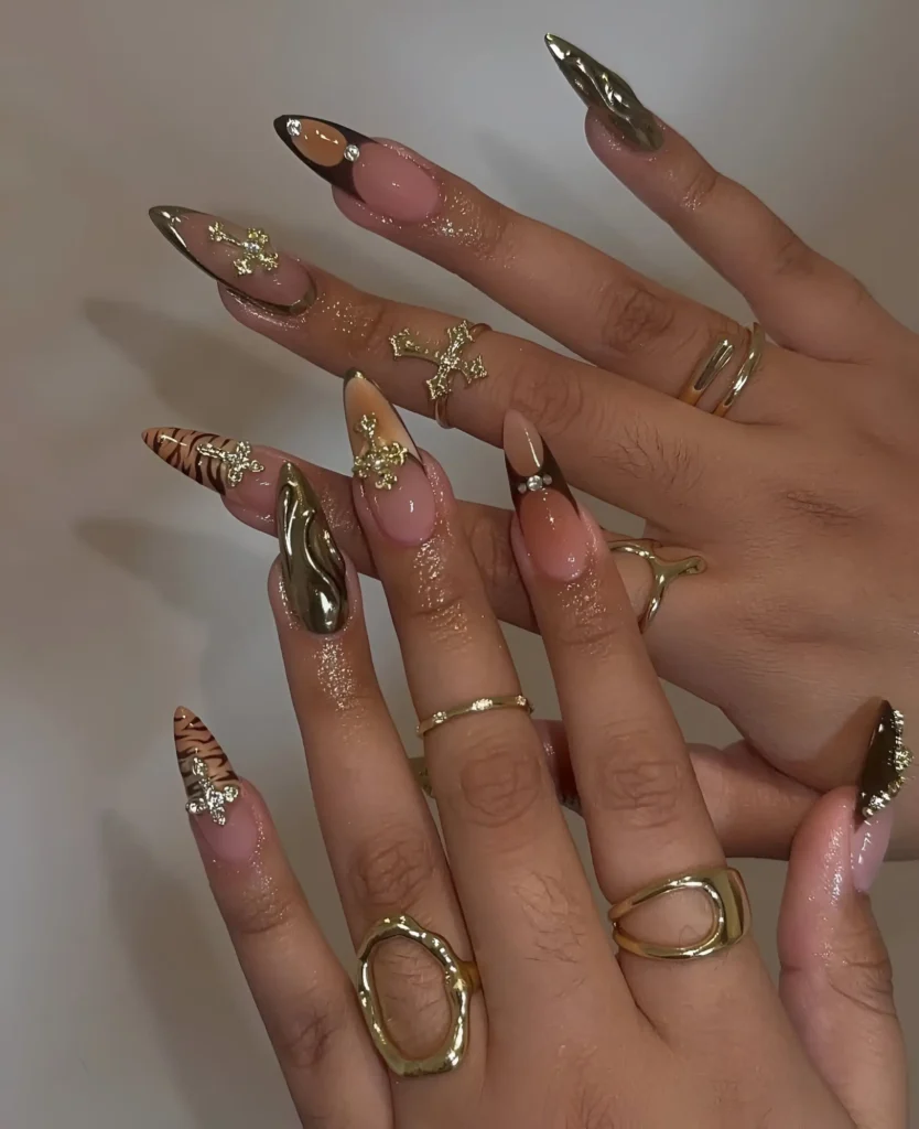 Maximalist stiletto nails combining tiger print tips, metallic texture, and ornate 3D cross charms.