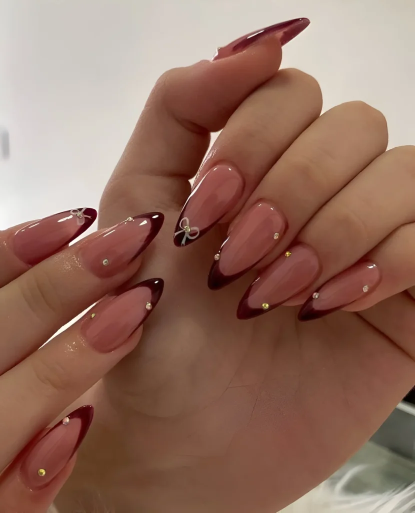 Deep V-shaped French manicure in glossy burgundy with delicate gem accents on long almond nails.