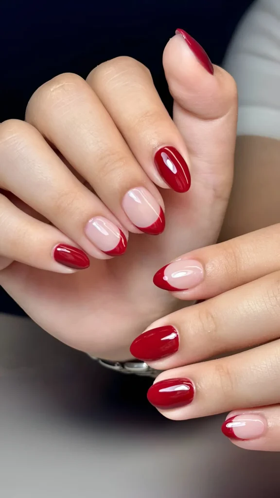 Rounded nails with glossy red polish and modern curved red tip design on a clear base.
