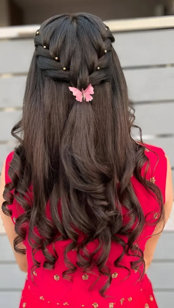 Back view of long dark hair in a half-up style with bead-accented braids meeting above flowing curls, featuring a pink butterfly clip.