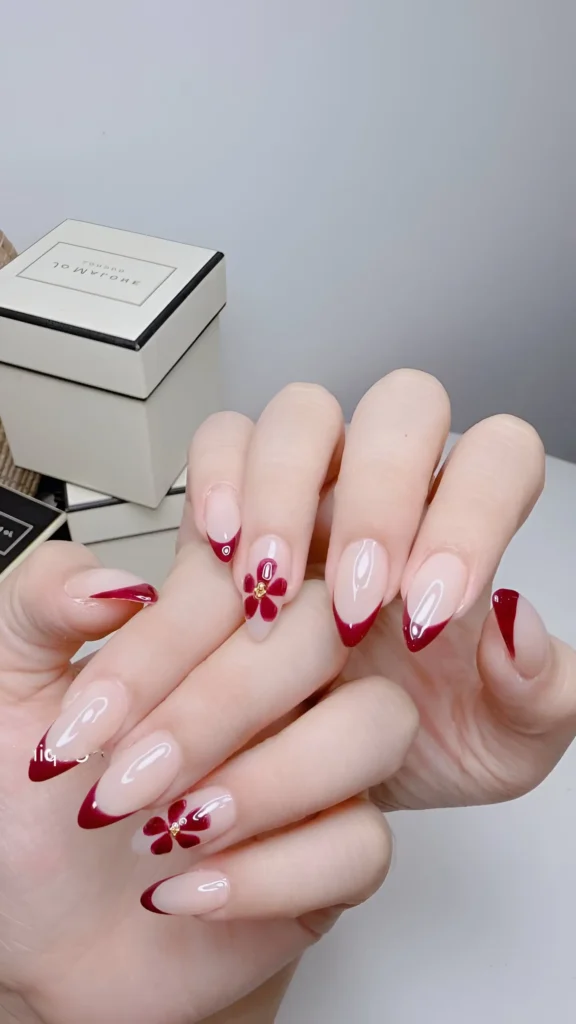 Deep burgundy French tips create an elegant look on long almond nails, accented with a matching floral detail. This is a sophisticated, classy nail idea.