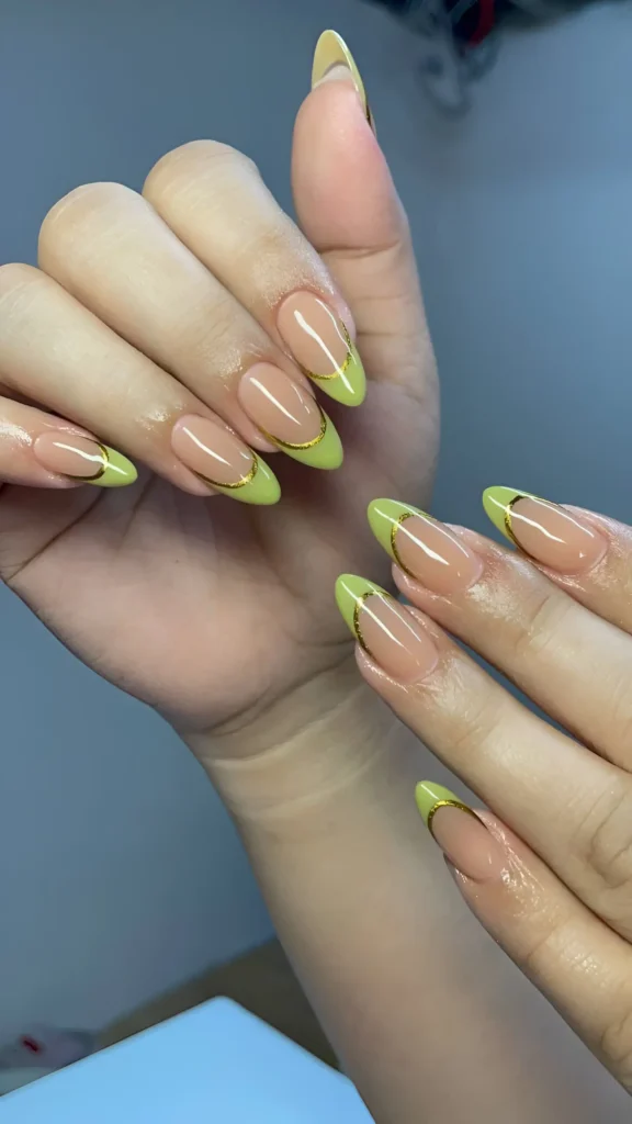 Almond-shaped nails with a sheer nude base, chartreuse green French tips, and a thin gold line accentuating the smile line.
