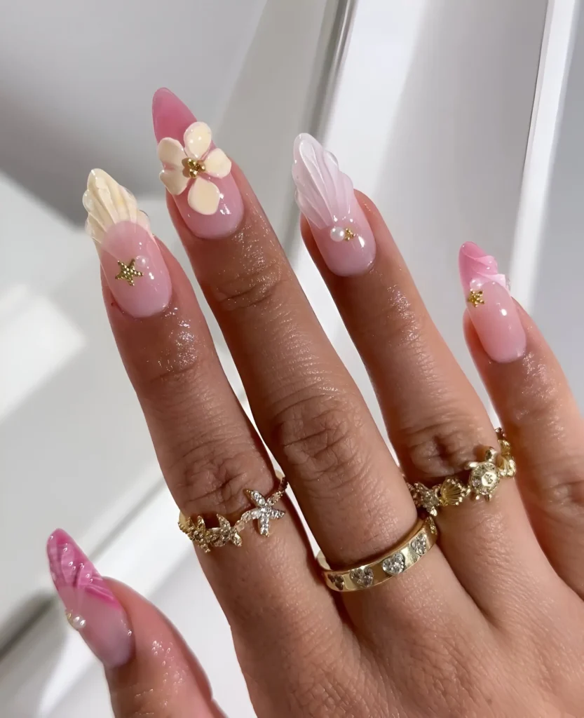 Long almond nails with a sheer pink base featuring large 3D sculpted flowers, shells, and bows in cream and pink with gold and pearl accents.