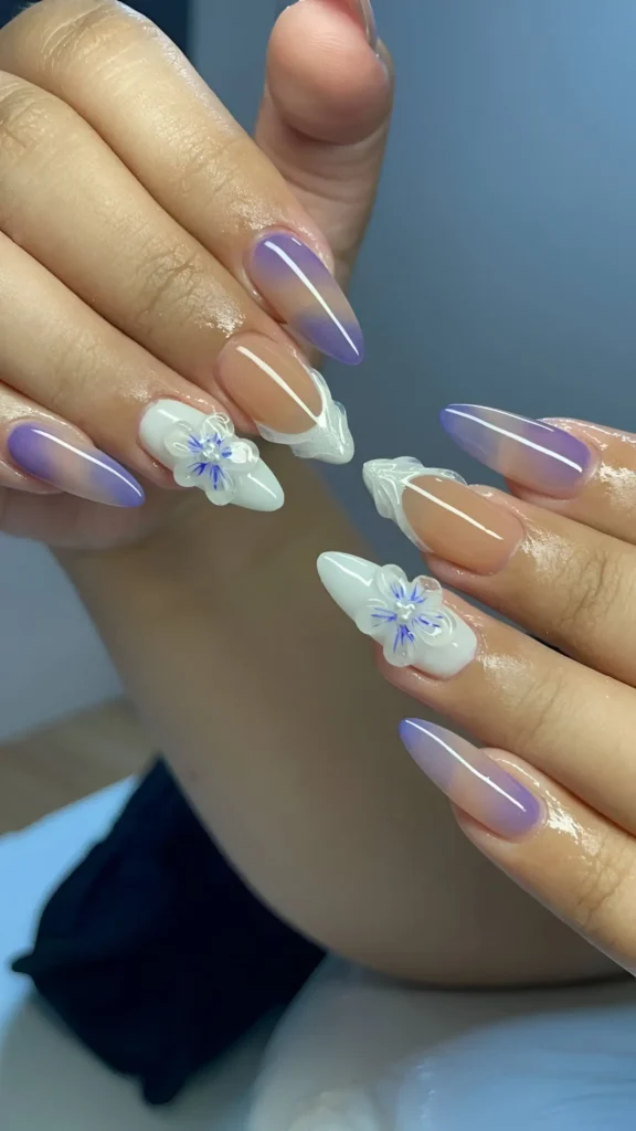 Stiletto nails featuring lavender purple ombré tips on a sheer base, mixed with white accent nails showcasing 3D white flowers with blue centers.