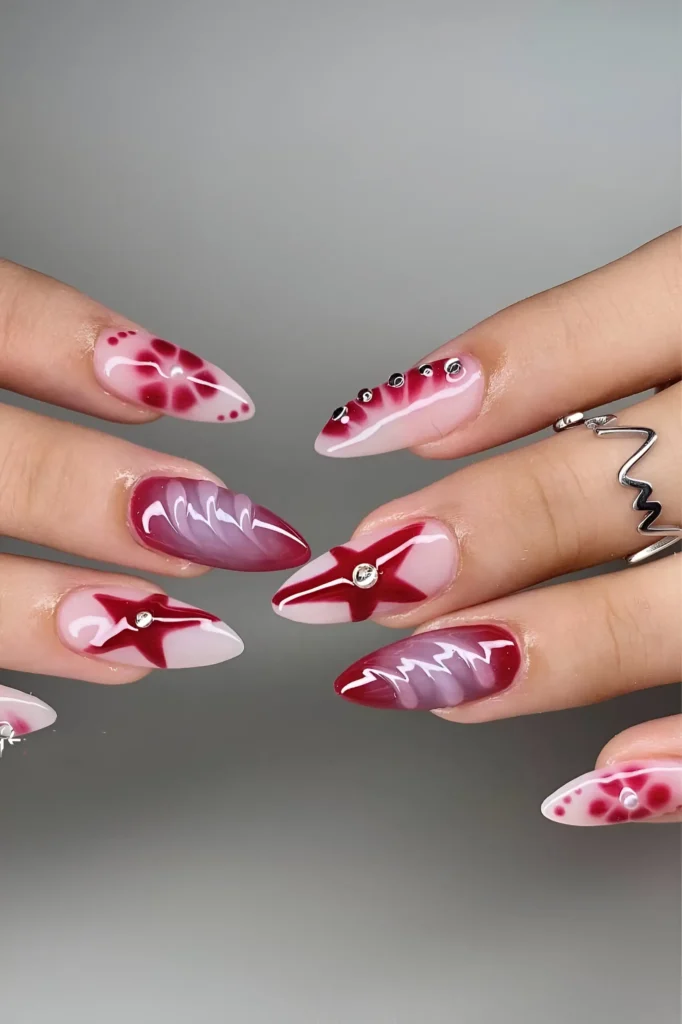 Long stiletto nails with mixed abstract red nail art including stars, smoky effects, and rhinestones.