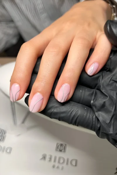 Short rounded nails with an opaque pale pink base and minimalist silver swirl line art.