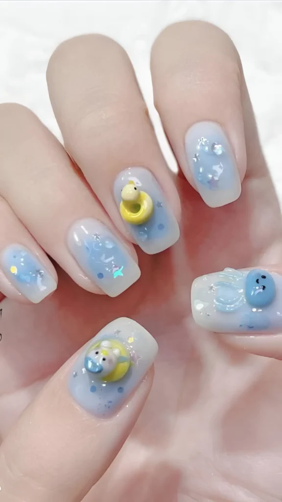 Playful short squoval nails with a milky blue glitter base and cute 3D rubber duck and blue bear charms.
