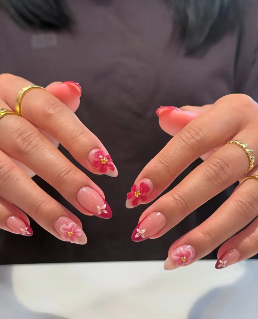 Almond nails featuring deep berry-colored French tips and coordinating 3D pink flowers with gold bead centers.