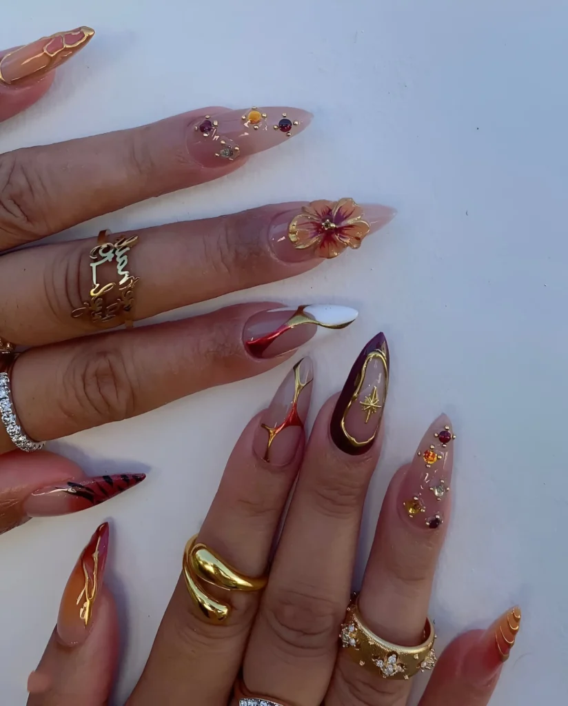 Eclectic nail art mix with celestial starbursts, fiery abstract lines, scattered gems, and 3D flower on stiletto nails.