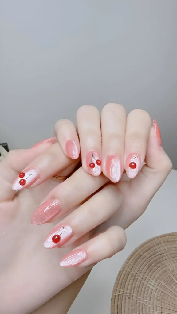 Almond nails with a shimmery pearlescent pink base and delicate red cherry motif accents.