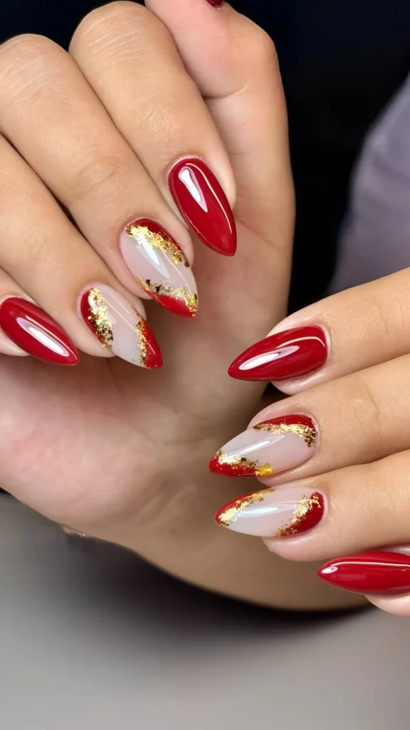 Almond nails with deep red polish and abstract red tips accented with gold foil.