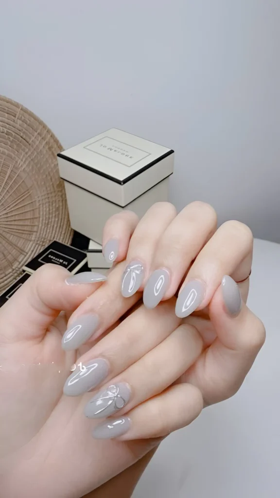 Minimalist light grey manicure with white bow accent on almond-shaped nails, showcasing subtle classy nail ideas.