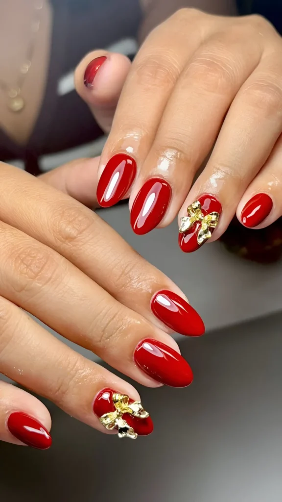 Oval nails with glossy red polish featuring large gold 3D bow charms on accent nails.