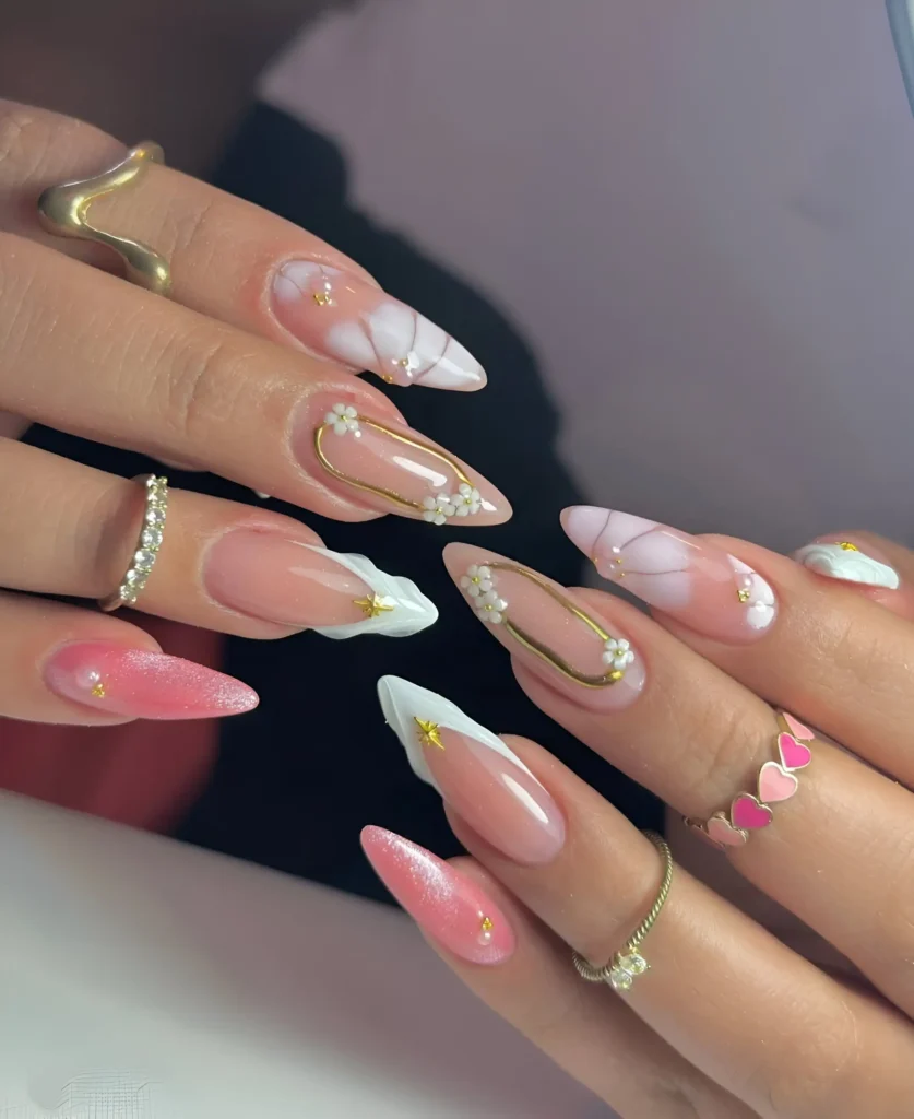 Long almond nails mixing sheer bases with white floral clusters, gold line details, white V-tips, and shimmery pink accents.