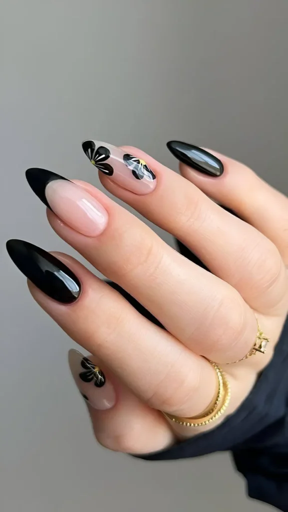 Long almond nails with a mixed design including solid glossy black nails and sheer nails decorated with black stylized flowers.