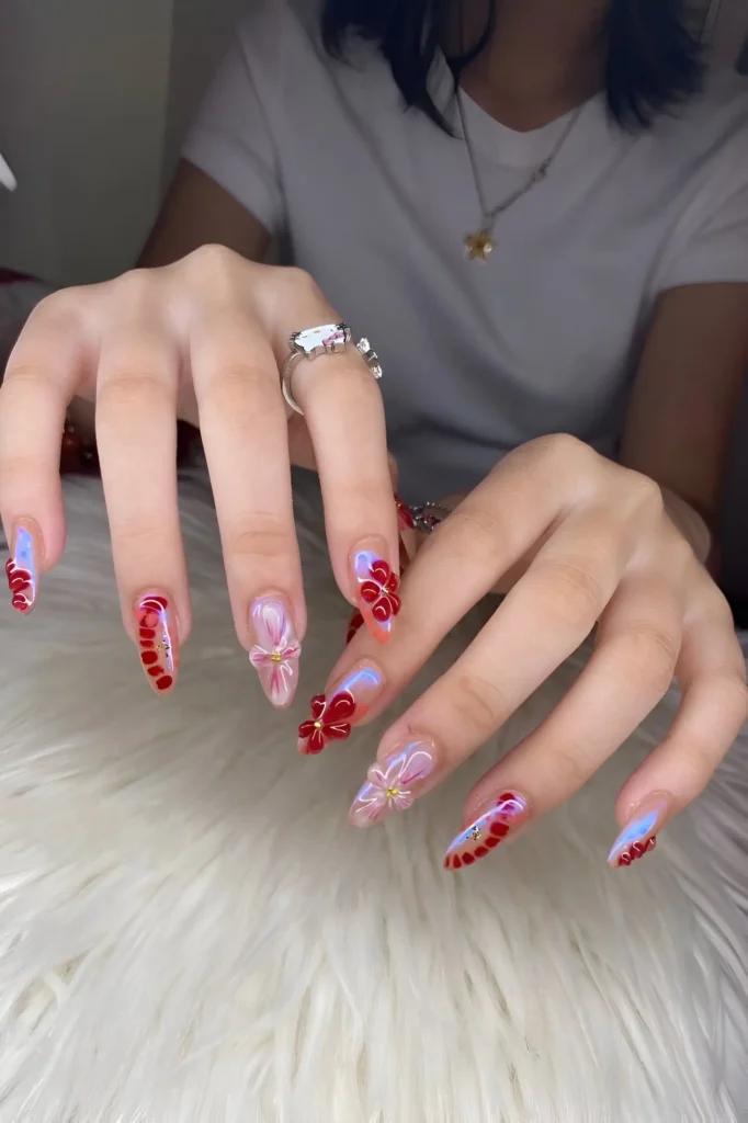 Summer nails with mixed art: 3D pink and red flowers, abstract red waves with gold beads, and light blue accents.