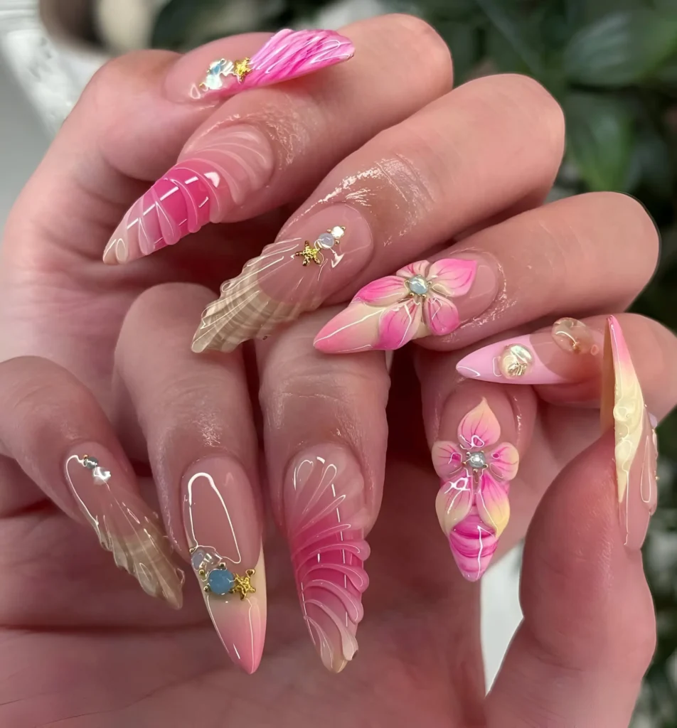 Long almond nails with bright pink and cream 3D textured shells and flowers, accented with gem clusters and gold stars.