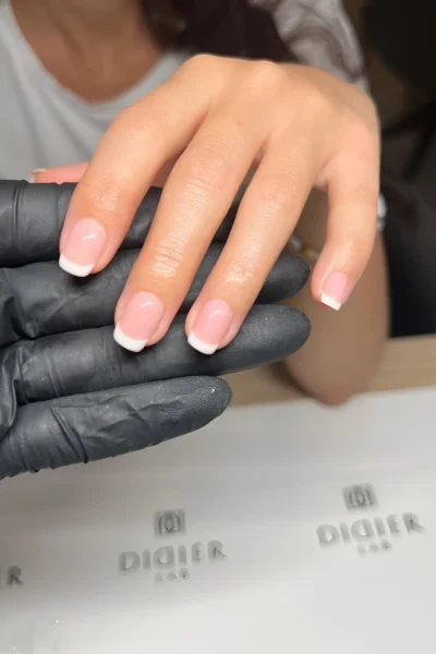 Short square nails with a classic French manicure featuring a sheer pink base and slightly thicker white tips.
