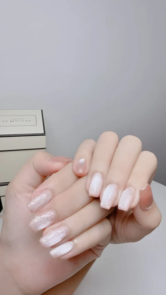 Frosted pearlescent white shimmer polish on short nails contrasted with a warm nude accent nail. An understated classy nail design.