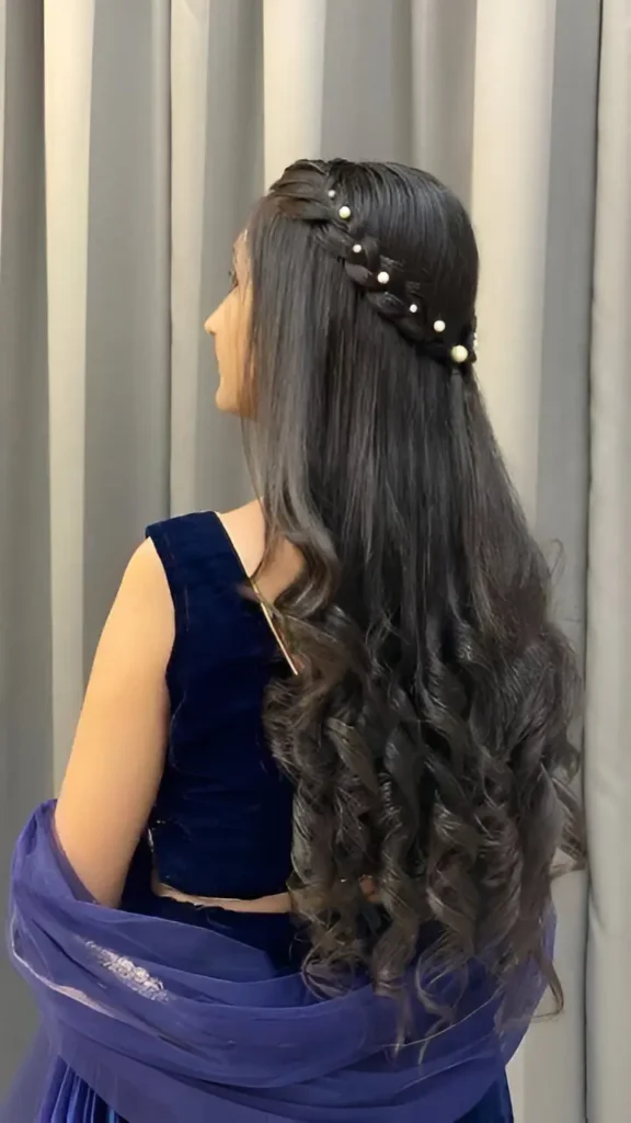 Side-back view of long dark hair in a half-up style featuring a pearl-accented braided headband and voluminous curls below.
