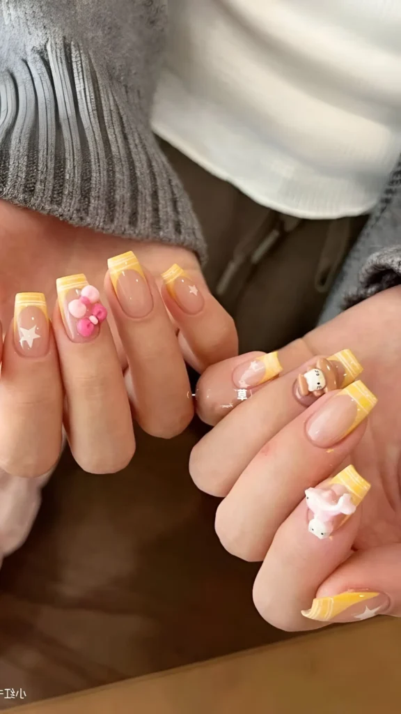 Medium-length square nails with pastel yellow French tips, adorned with large 3D charms including a flower, a white character, a brown bear, and small painted stars.