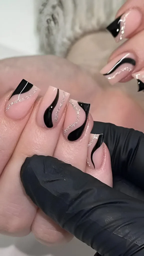 Square nails with a sheer nude base decorated with abstract glossy black swirls and fine silver glitter lines.