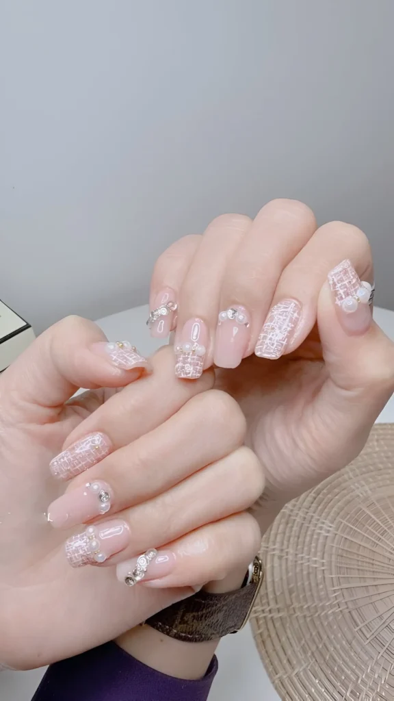 Sophisticated tweed pattern nail art in white on pink base, adorned with pearls and crystals – a unique classy nail design.