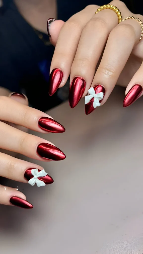 Long almond nails with metallic red chrome finish and matte white 3D bow accents.