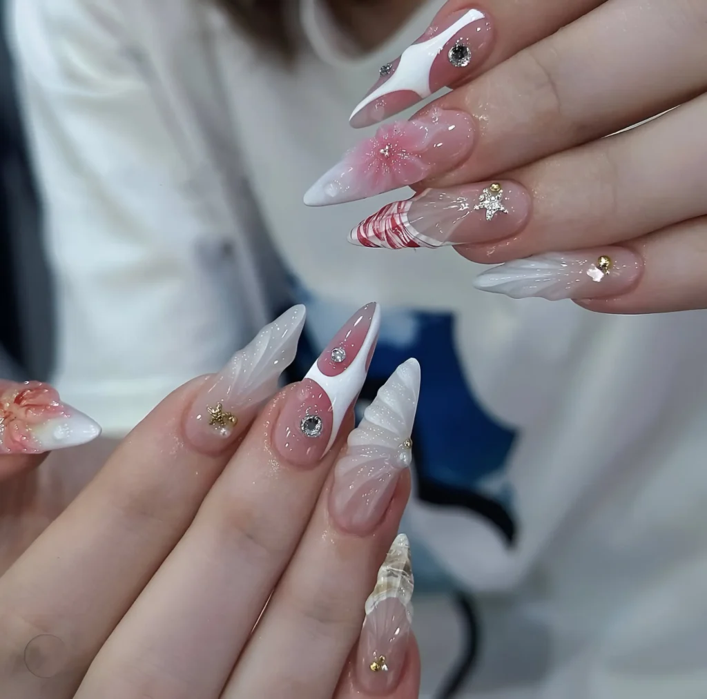 Long almond nails mixing sheer base with bold white abstract shapes, 3D textures (white and shell), stripes, and assorted gem and gold star accents.