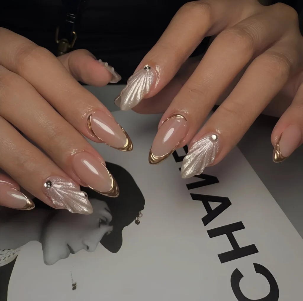 Almond nails alternating between gold metallic outlines on a nude base and pearlescent white 3D textured designs with a single gem.