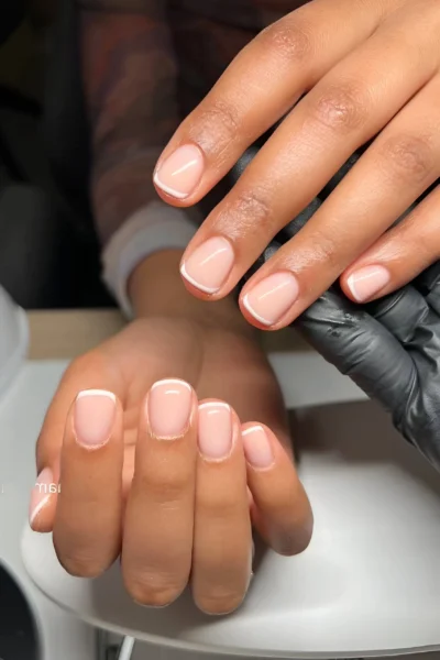 Short square nails with a micro French manicure featuring a sheer base complementing skin tone and fine white tips.