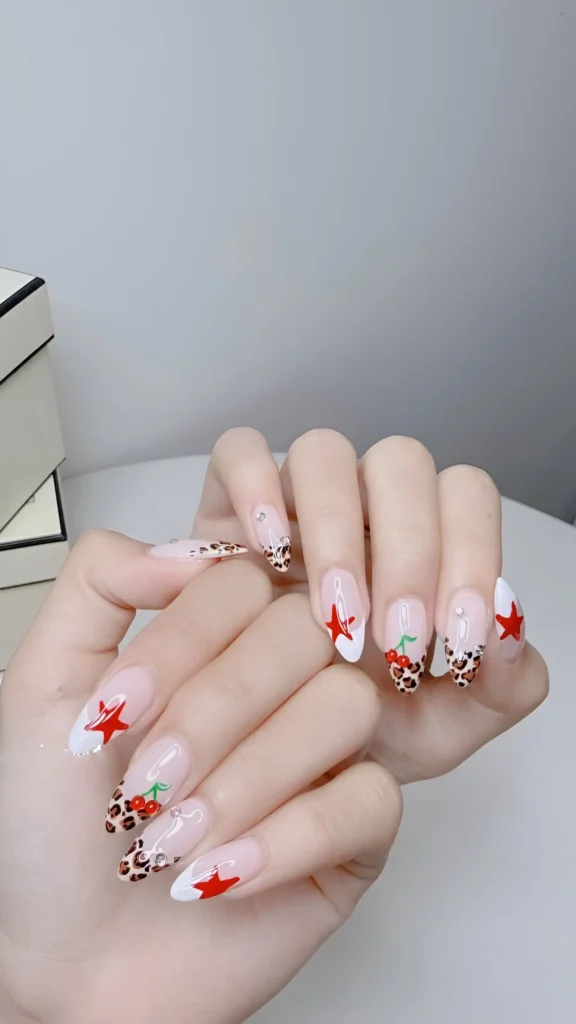 Bold nail art mix: leopard print French tips, red stars, cherry motifs, and crystals on long almond nails.