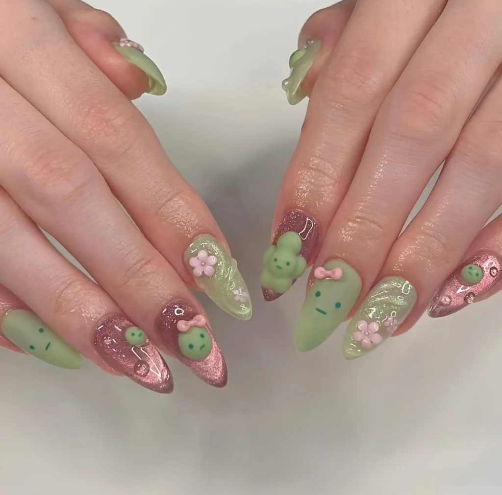Playful 3D kawaii character art with green figures, pink flowers, and bows on glitter and matte nails.