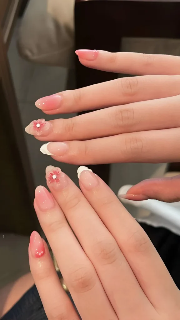 Delicate nail design combining white French tips, sheer rosy jelly polish, and small 3D pink flowers with crystal centers.