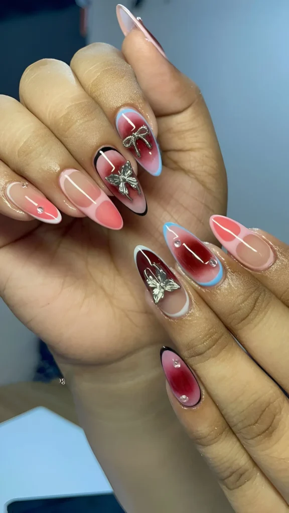 Almond nails featuring multi-color aura designs (burgundy, coral) on a sheer base, with black outlines, blue tips, silver bows, gems, and dewdrops.
