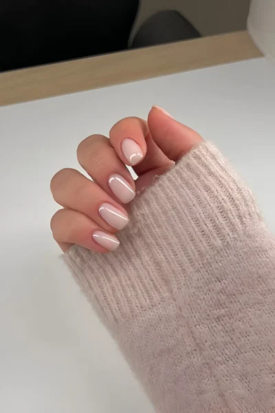 Short rounded nails with an opaque creamy nude polish, one featuring a subtle white cuticle crescent detail.