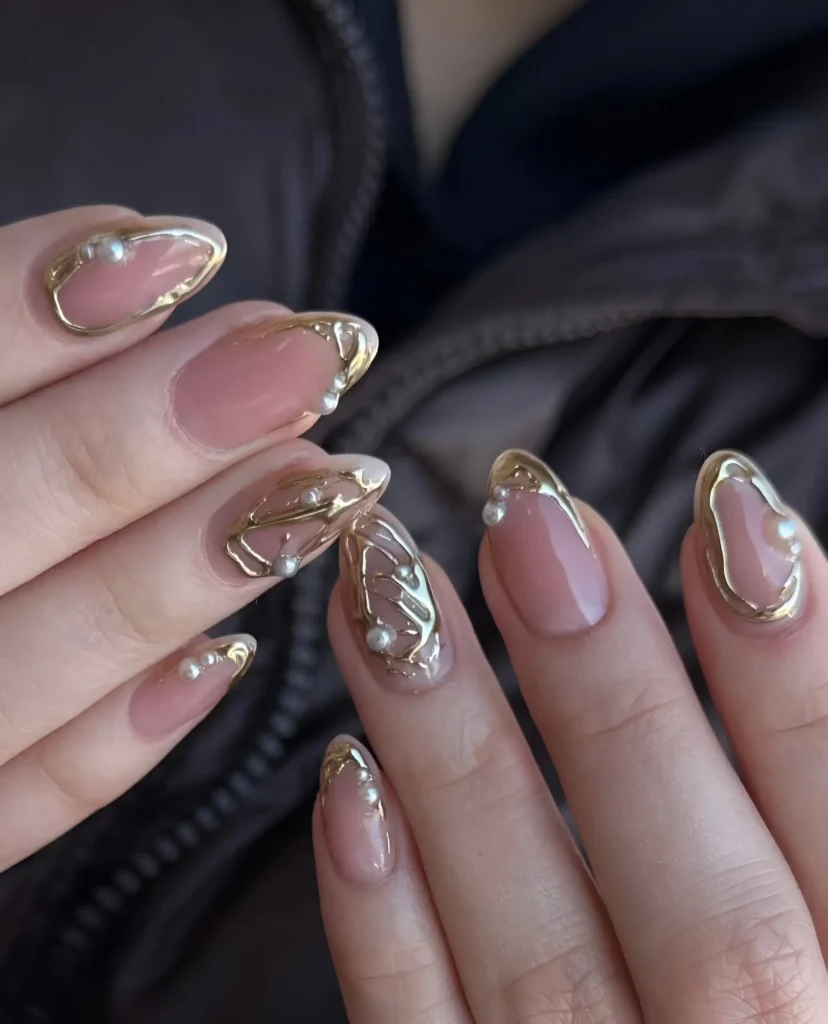 Almond nails with sheer nude base featuring delicate 3D gold line swirls and outlines accented with pearls.
