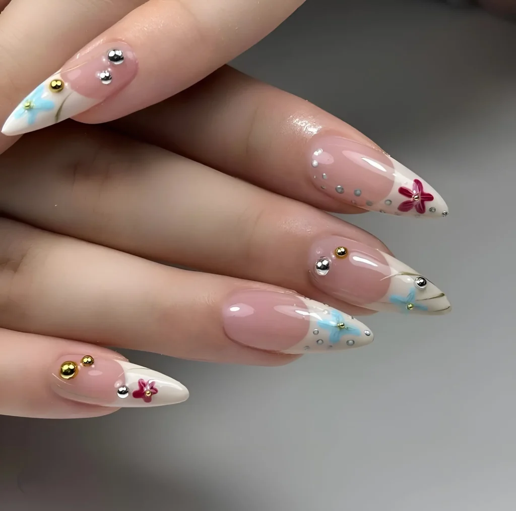 Elegant French manicure with tiny painted flowers and gold linework on tips, accented with mixed-metal studs.