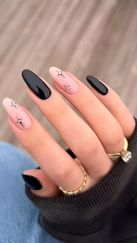 Long almond nails featuring a mix of solid glossy black nails and sheer nails decorated with black starburst graphics.